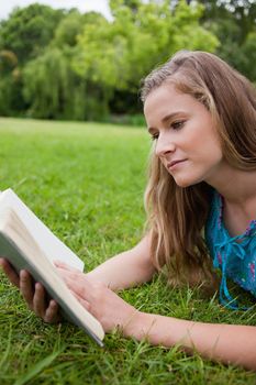 Serious young girl reading a book while lying on the grass in a parkland