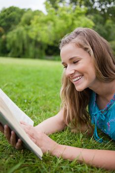 Young girl reading a book in a parkland while lying on the grass and laughing