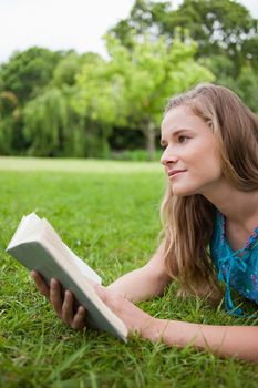 Thoughtful young woman holding a book while looking away and lying on the grass