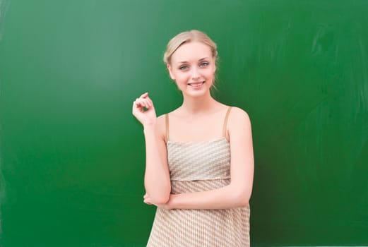 beautiful young teacher is standing near blackboard and looking at the camera