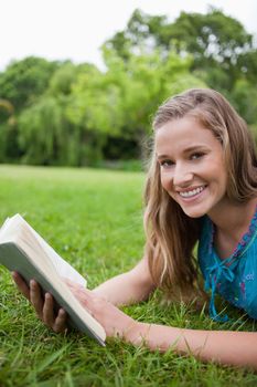 Happy student lying on the grass in the countryside while holding a book