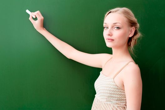 young beautiful teacher writes on the blackboard with chalk