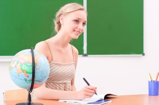 portrait of beautiful young teacher, sits at a desk in the classroom