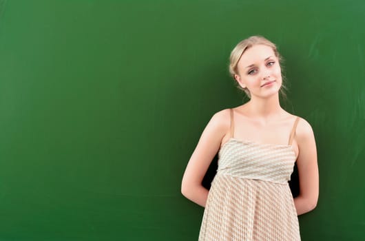 beautiful young teacher is standing near blackboard and looking at the camera