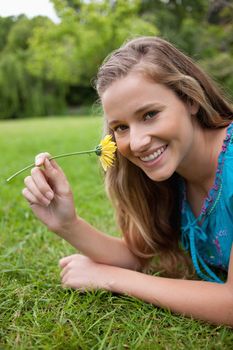 Young smiling woman smelling a yellow flower while lying down in the countryside