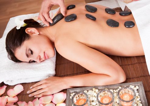 Beautiful young woman getting hot stone therapy at spa salon