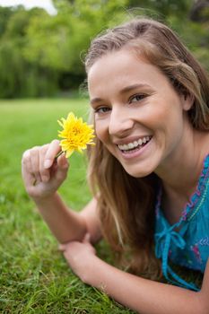 Smiling teenager holding a beautiful flower while lying on the grass in the countryside