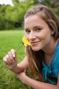 Happy student lying in a parkland while smelling a flower and looking at the camera