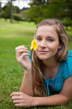 Young relaxed woman holding a beautiful yellow flower while lying in the countryside