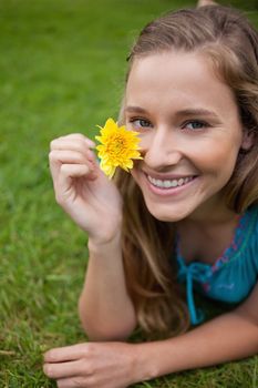 Smiling young girl showing a beautiful yellow flower while lying on the grass in a park