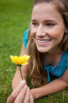 Young smiling woman looking away while lying in a park and holding a yellow flower