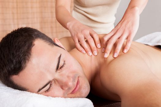 Cheerful young man getting shoulder massage at spa