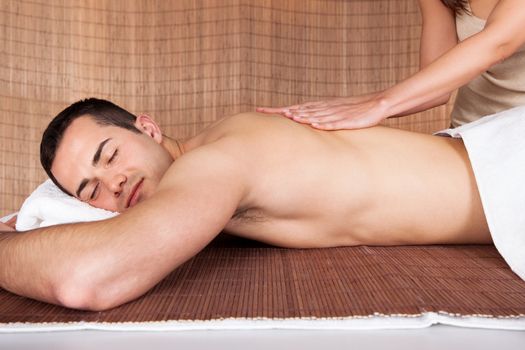 Cheerful young man getting shoulder massage at spa