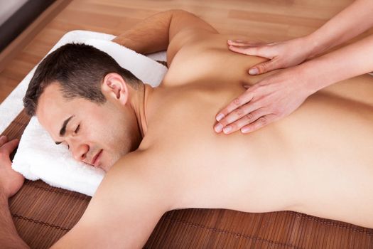 Cheerful young man getting shoulder massage at spa