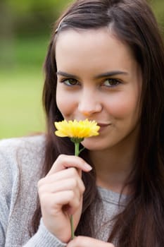 Young woman looking at the camera while standing upright and smelling a flower