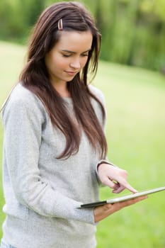 Serious young woman standing up in the countryside while using her tablet pc