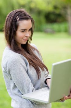 Young relaxed woman holding her laptop while standing upright in the countryside
