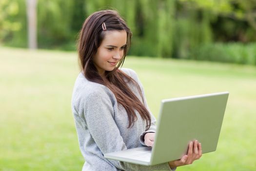 Serious young girl standing in a public garden while working on her laptop