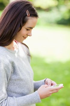 Relaxed young woman sending a text with her cellphone while standing in a park