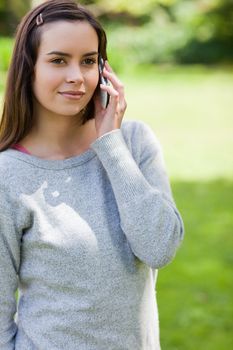 Young serious adult calling with her mobile phone while standing in a parkland