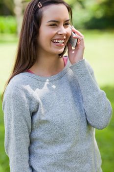 Young girl standing in a parkland while talking on the phone and laughing