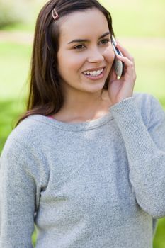 Young girl talking with her cellphone while standing in a parkland