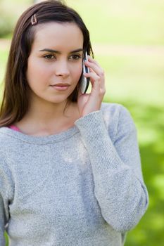 Serious young woman calling with her cellphone while standing upright in a park