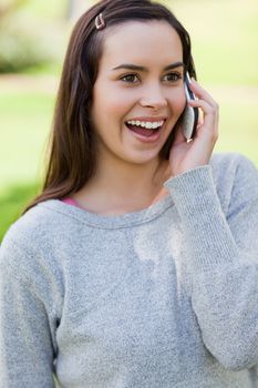 Young woman showing her surprise while talking on the phone and standing in a park