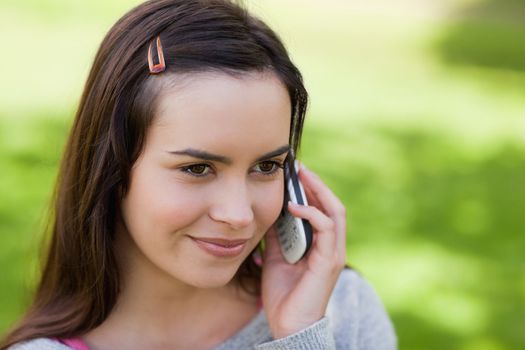 Young relaxed girl talking on the phone while standing upright in a parkland