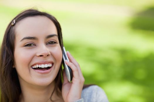 Young laughing woman standing upright in a parkland while talking on the phone