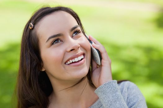 Young smiling woman talking with her cellphone while looking up in the countryside