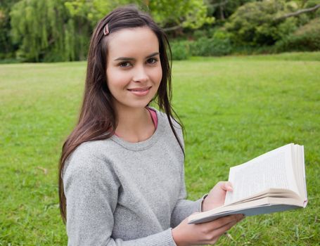 Smiling young girl standing in a parkland while holding a book