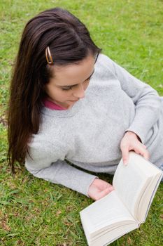 Young serious woman reading a book while lying down in a public garden