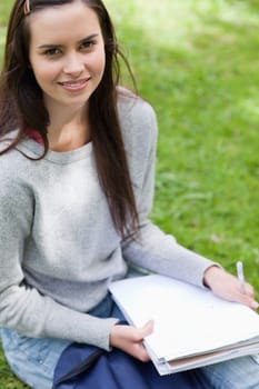 Happy student sitting in a park while looking at the camera and holding school books