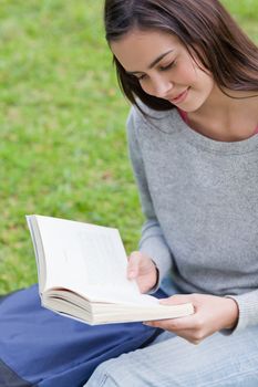 Young relaxed girl sitting on the grass in a parkland while reading a book