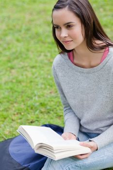 Young calm girl holding a book in a public garden while looking towards the side