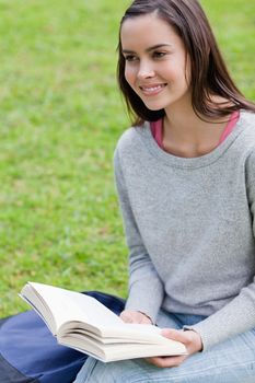 Smiling young girl looking away while holding a book in the countryside