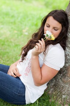 Young pretty woman leaning against a tree in the countryside while smelling flowers 