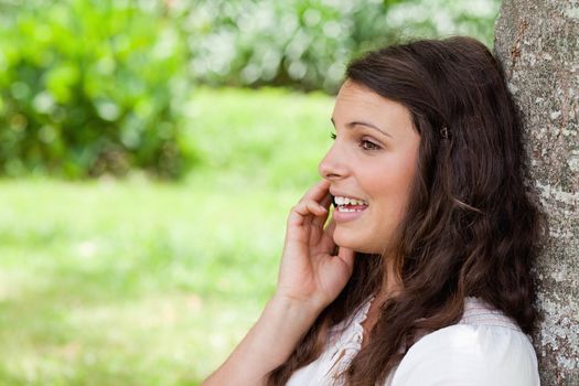 Young attractive woman talking with her mobile phone while leaning against a tree