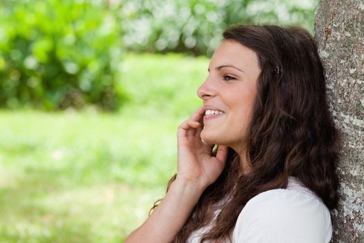Young happy girl leaning against a tree in the countryside while talking on the phone