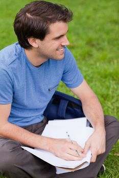 Young smiling man looking away while sitting on the grass in a park and working