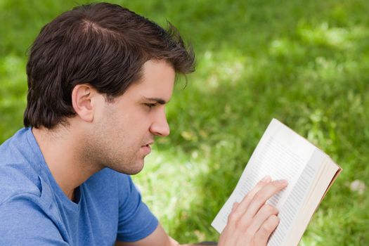 Young serious man reading a book while sitting down in the countryside