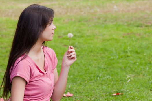 Young relaxed woman holding a dandelion while standing in a public garden