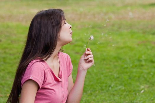 Young relaxed woman blowing a dandelion while standing in the countryside