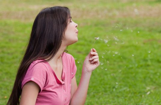Young woman standing upright in the countryside while blowing a dandelion