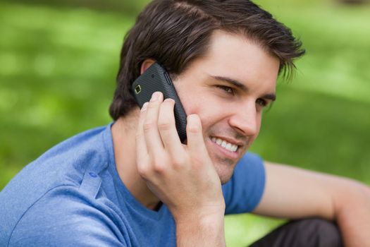 Smiling young man sitting in the countryside while talking with his mobile phone