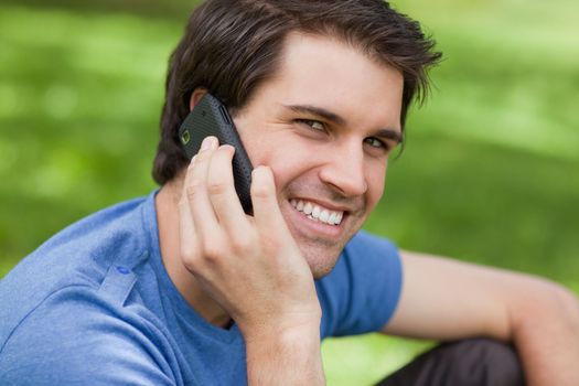 Smiling young man looking at the camera while using his mobile phone in a parkland