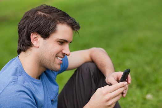 Young man sending a text with his mobile phone while sitting in a public garden