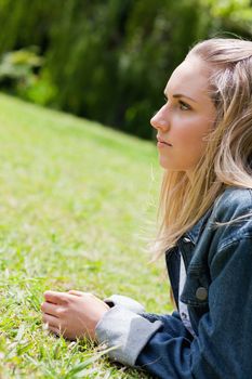 Young serious girl looking ahead while lying on the grass in the countryside