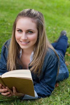 Young happy girl lying on the grass in the countryside while reading a book